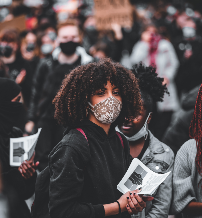 Person in a crowd wearing a mask and holding a pamphlet
